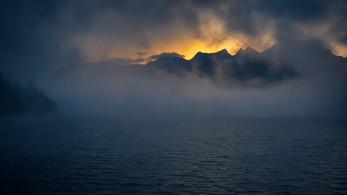 Lago patagónico al amanecer con bruma densa y la silueta de la cordillera al fondo