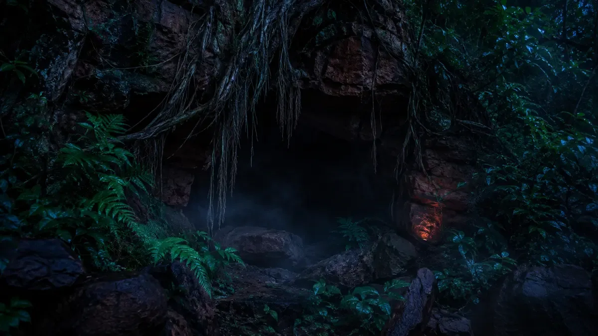 Entrada oscura de una cueva entre grandes piedras coloradas del monte con raíces colgando